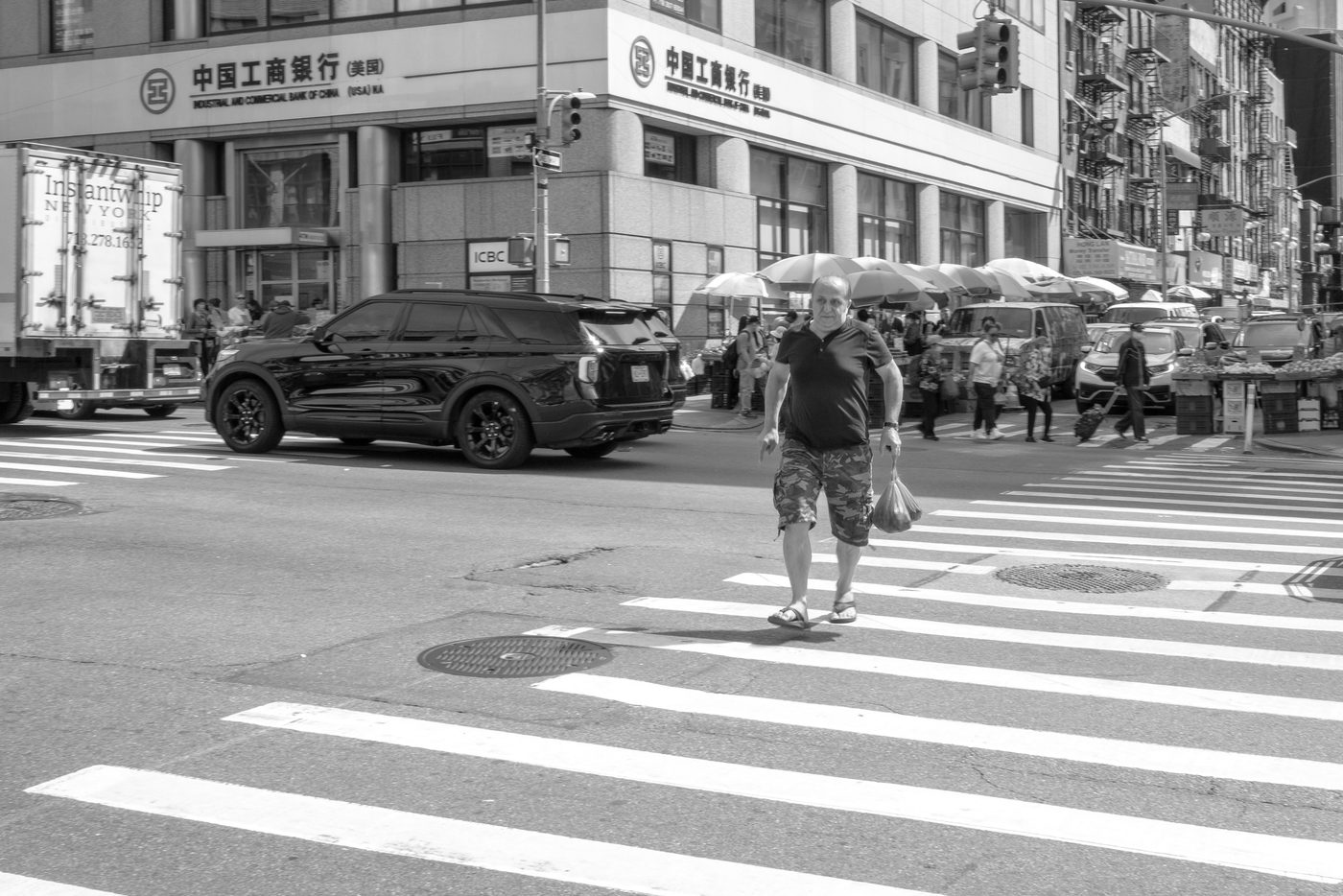 Man crossing the street with a plastic bag in front of a Chinese bank, New York