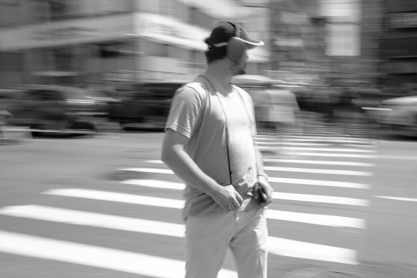 Blurred man in a cap and headphones crossing a crosswalk, New York