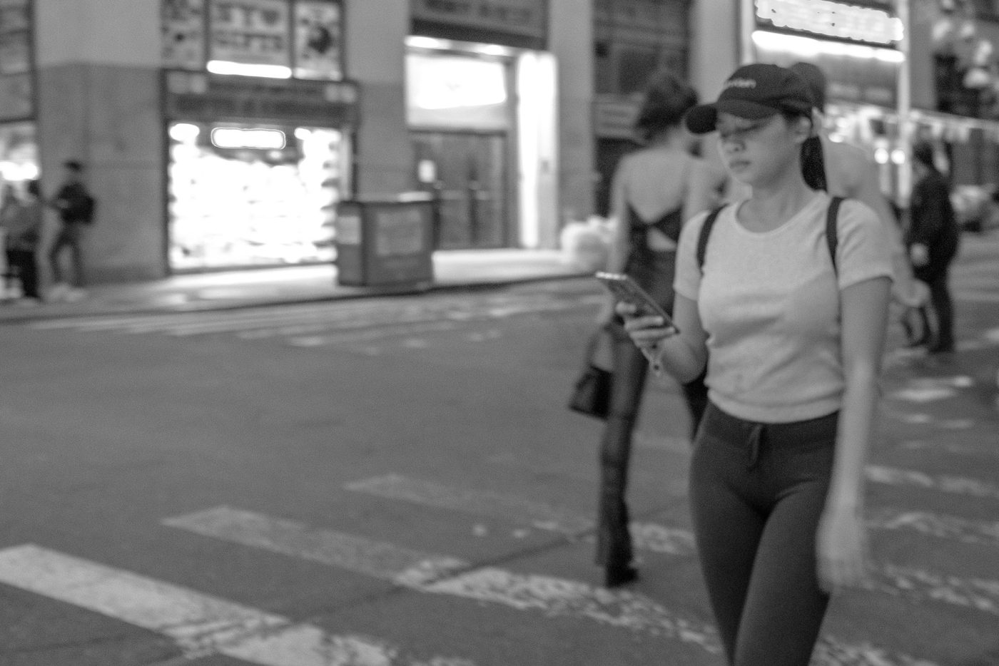 Woman on the phone walking at night, a blurred silhouette in the background, New York