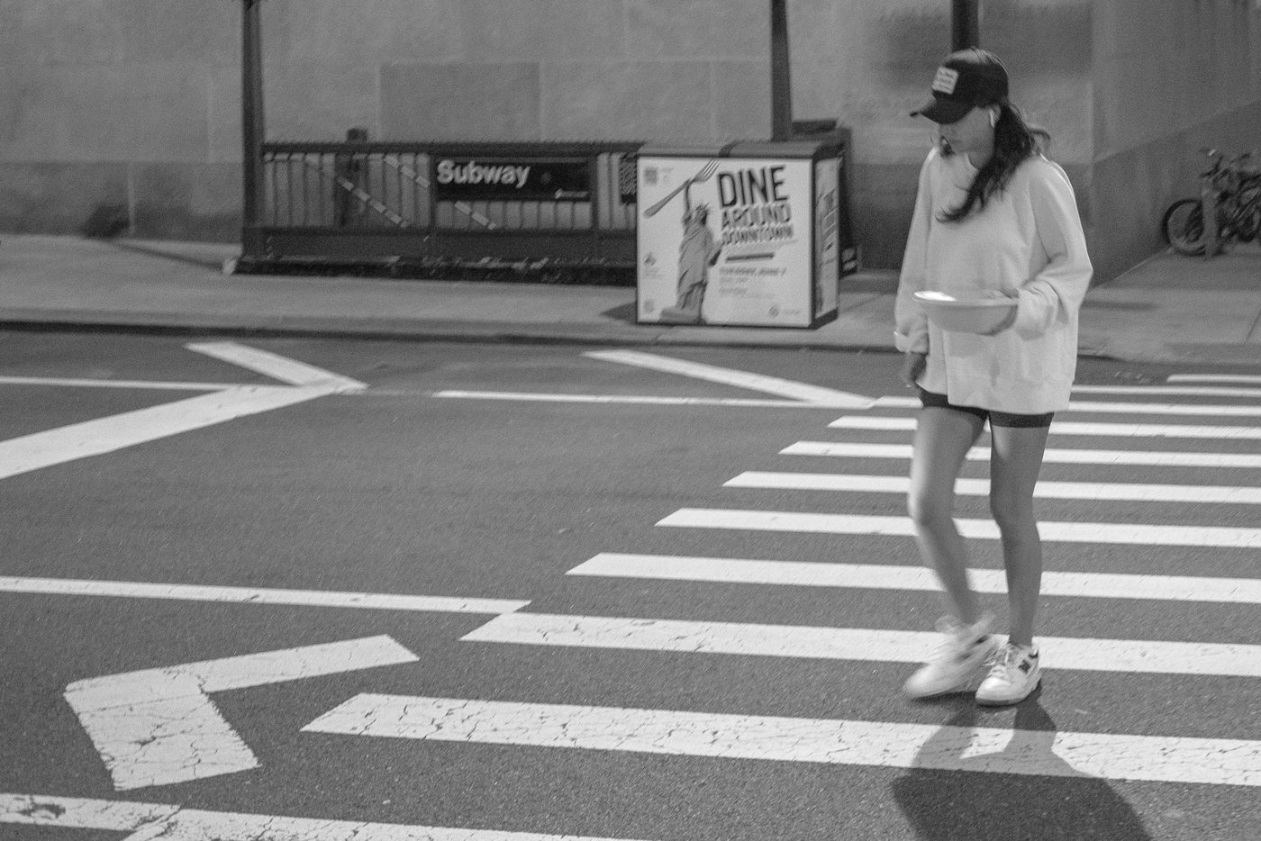 Woman in a cap crossing the street with a takeout meal at night, New York