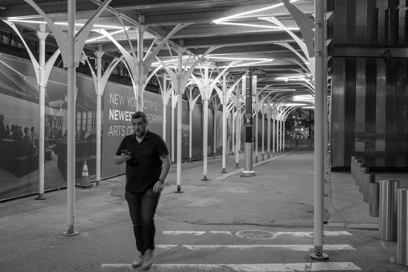 Man on the phone walking beneath a white metal archway at night, New York