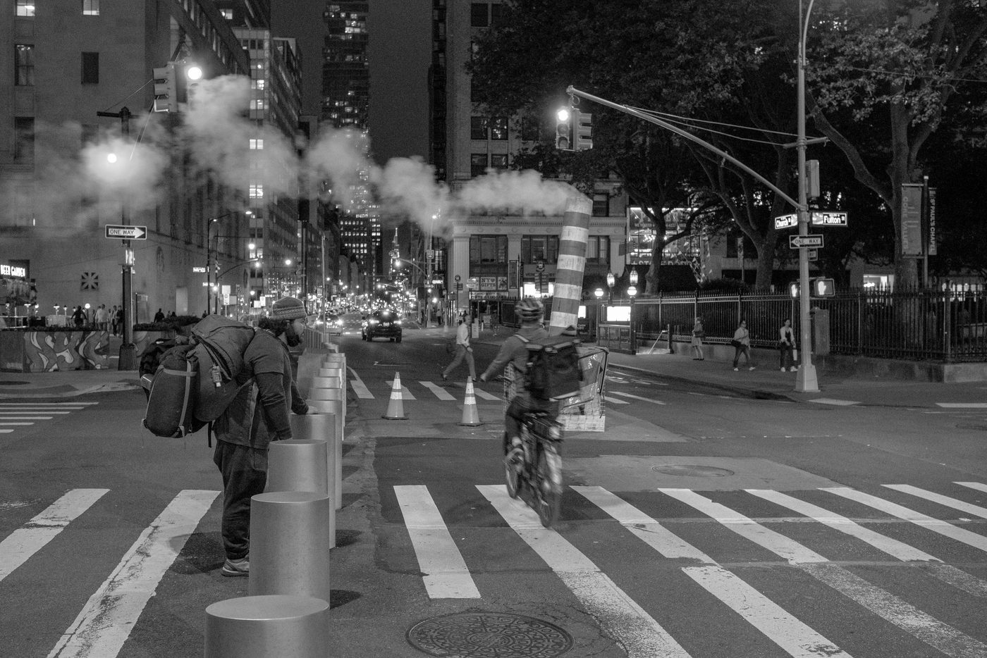Delivery cyclist crossing an intersection shrouded in steam at night, New York