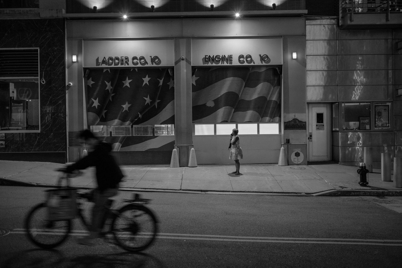 Woman standing in front of Ladder Co. 10 firehouse decorated with an American flag, New York