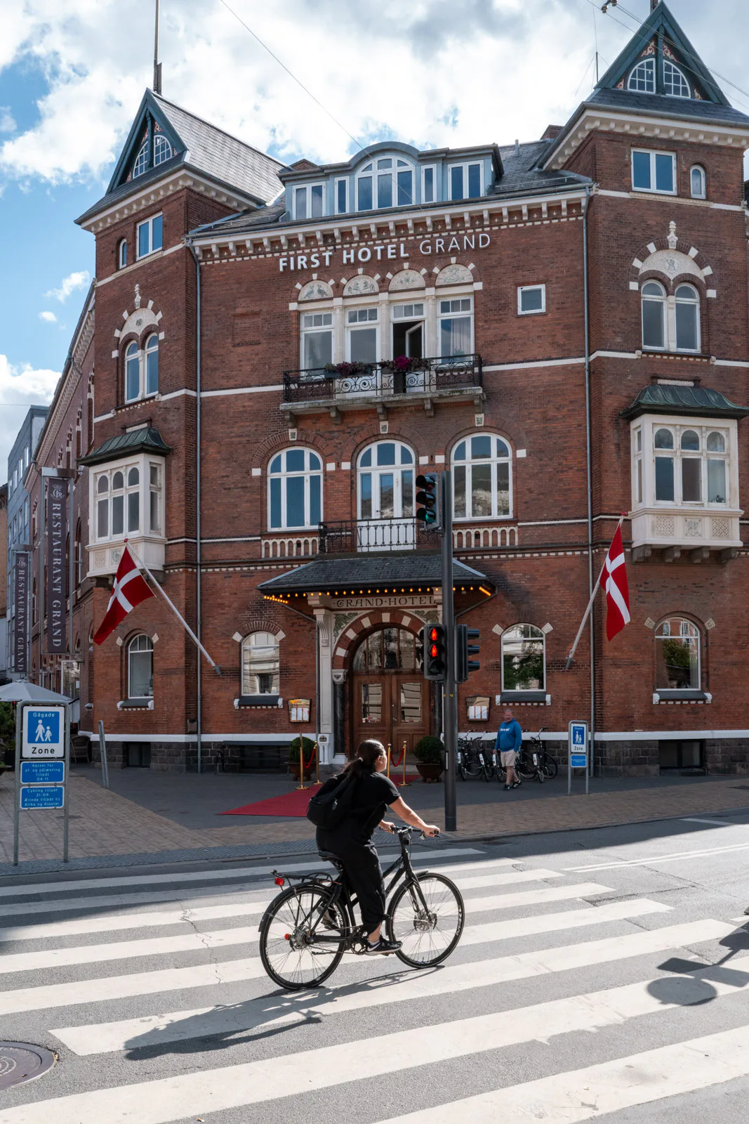 Un cycliste passe devant la façade de briques du First Hotel Grand, Odense