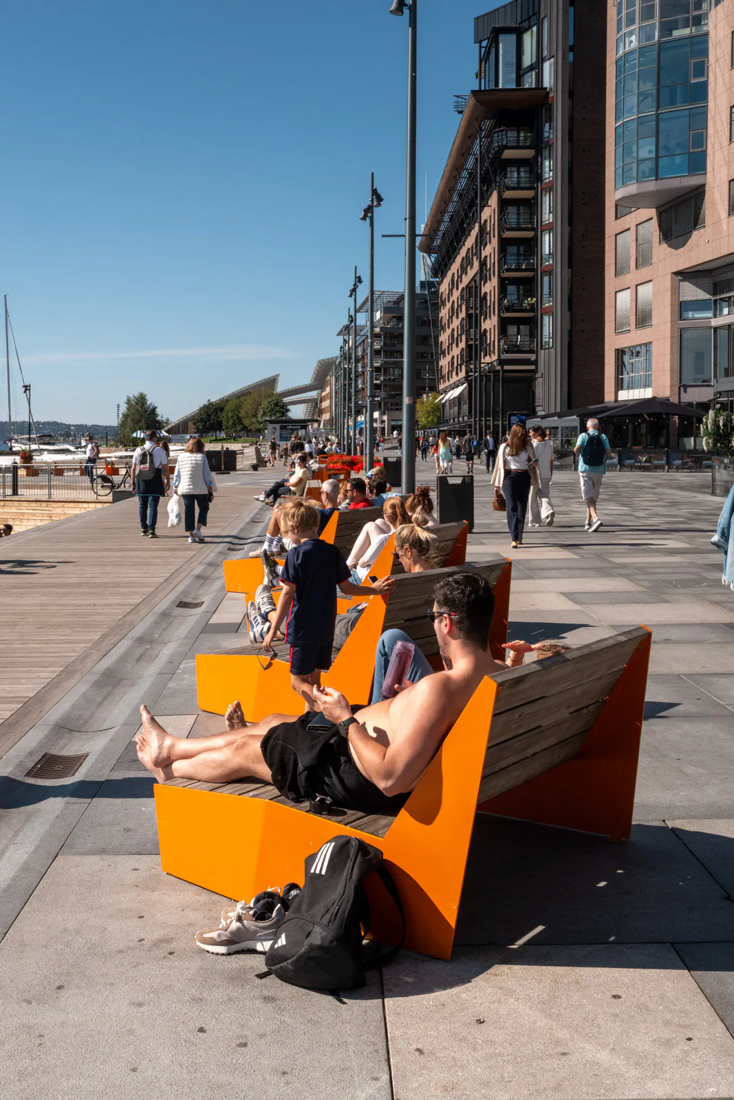 Des promeneurs au soleil sur les bancs orange du front de mer, Oslo