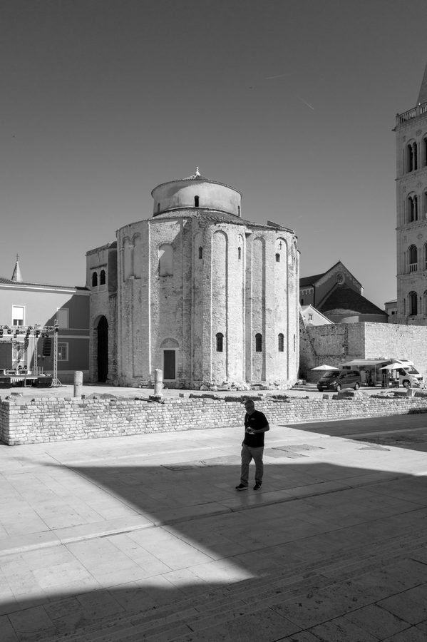 Passant traversant une place ensoleillee devant une eglise en pierre, Zadar