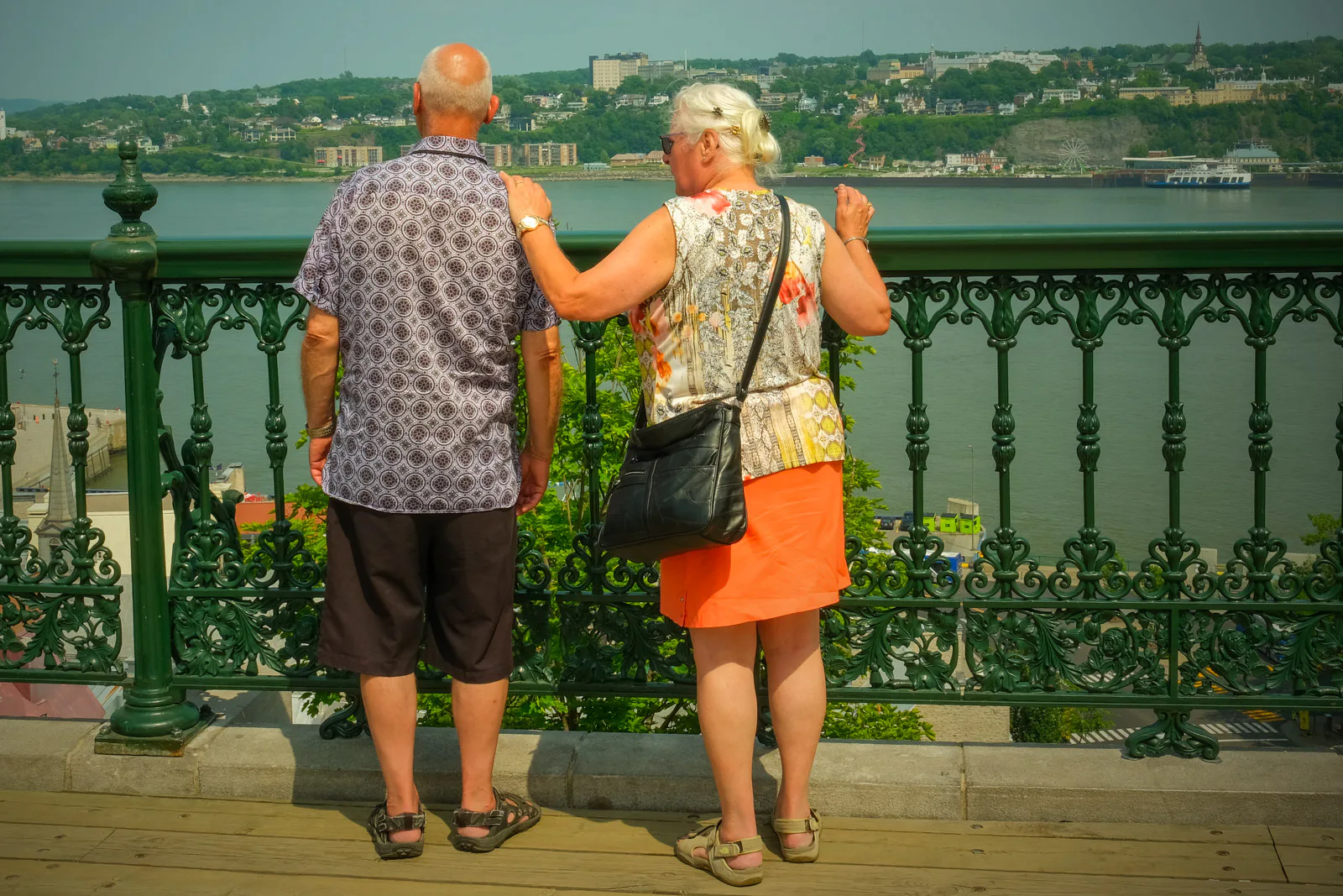 Un couple âgé accoudé à la rambarde de fonte verte, face au fleuve, Québec