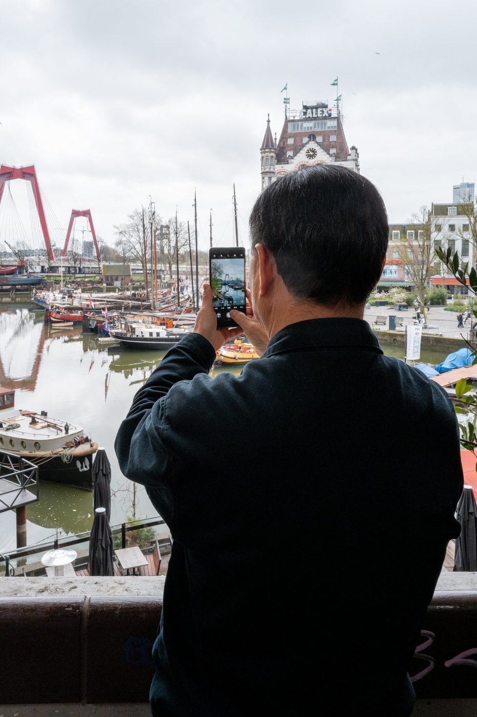 Tourist photographing the harbor and the Willemsbrug bridge with a phone, Rotterdam