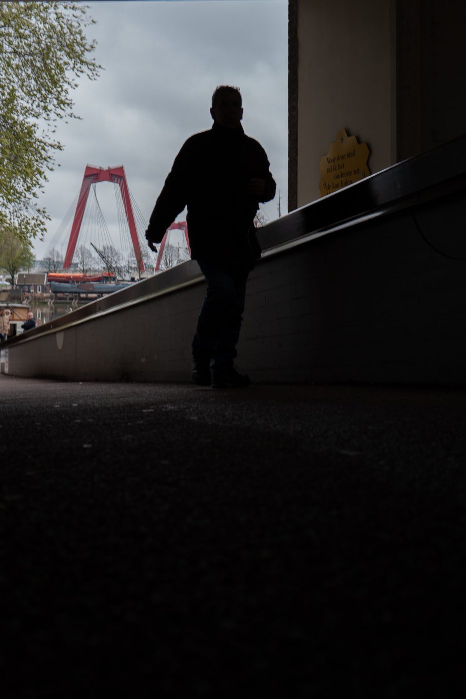 Silhouette of a man walking along a railing facing the red bridge, Rotterdam