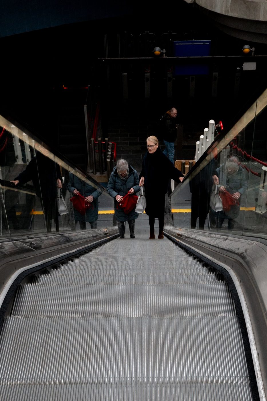 Three women going down an escalator with red bags, Rotterdam