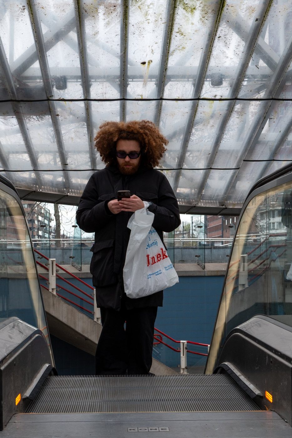 Young man with curly hair on an escalator with a plastic bag, Rotterdam