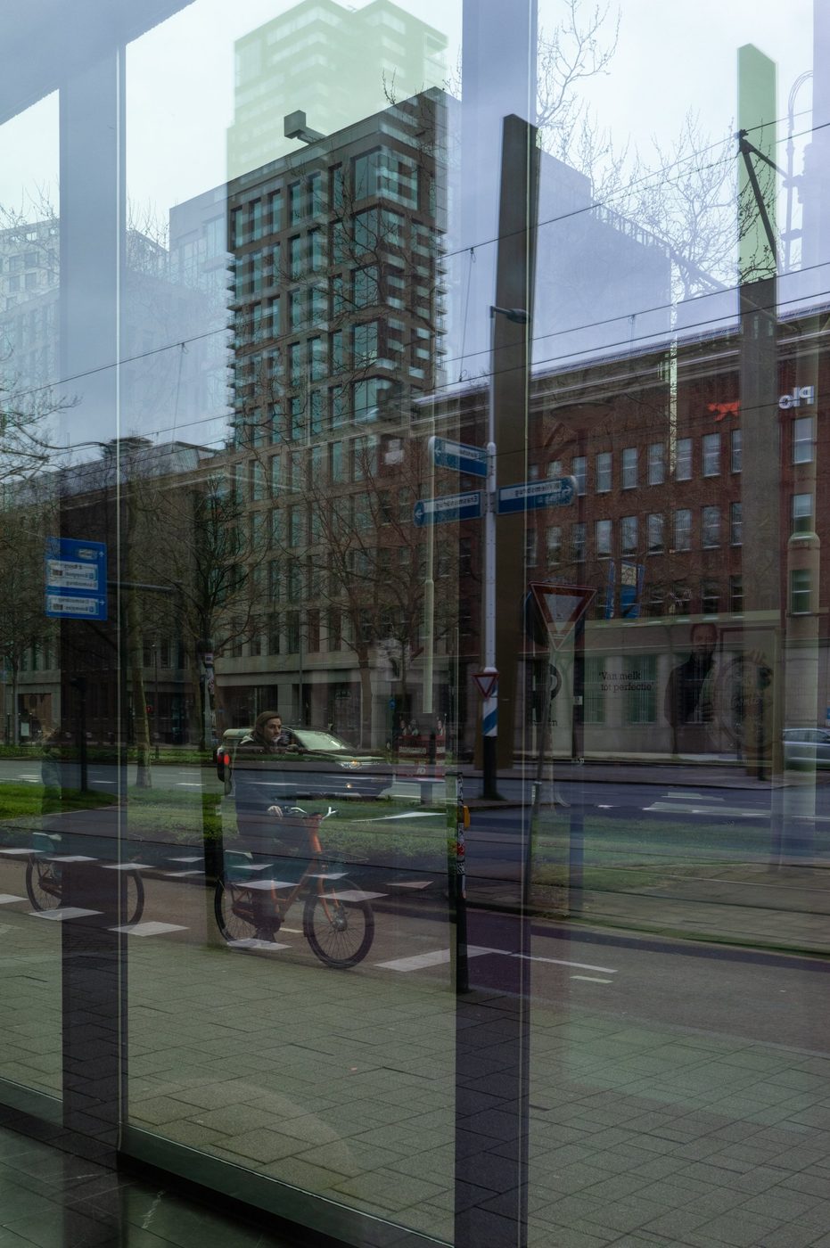 Glass storefront reflecting a building and a cyclist, Rotterdam