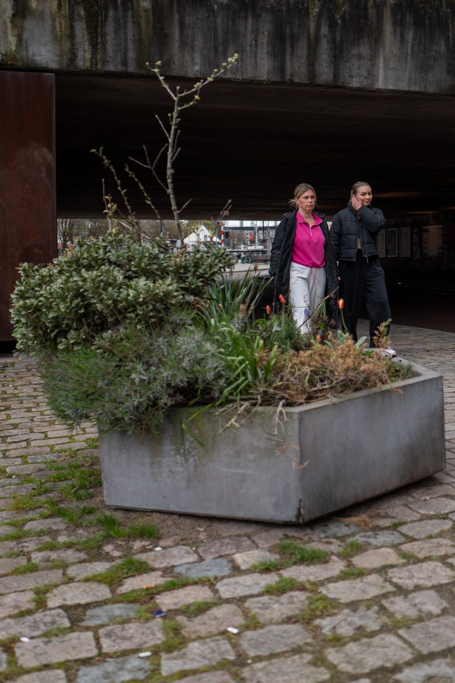 Two women walking past a large planter under a bridge, Rotterdam