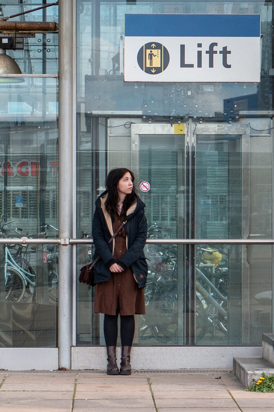 Woman waiting near a lift sign and a bicycle parking area, Rotterdam