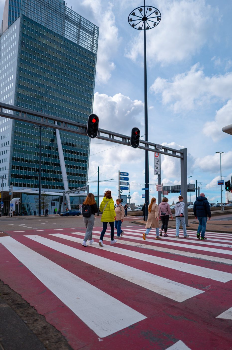 Pedestrians crossing a red and white crosswalk near a tower, Rotterdam
