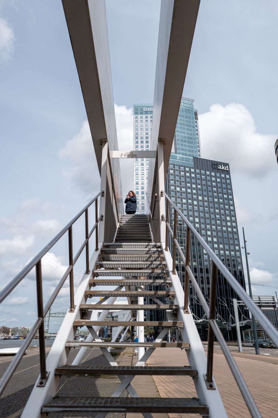 Visitor photographing from a metal staircase facing the city center towers, Rotterdam