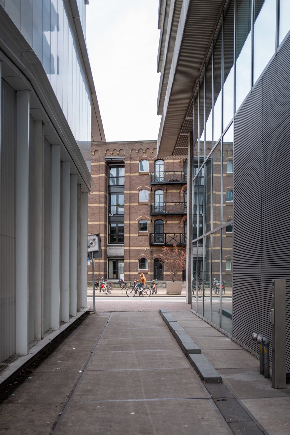 Glass-walled alley with a cyclist glimpsed in the distance between two buildings, Rotterdam