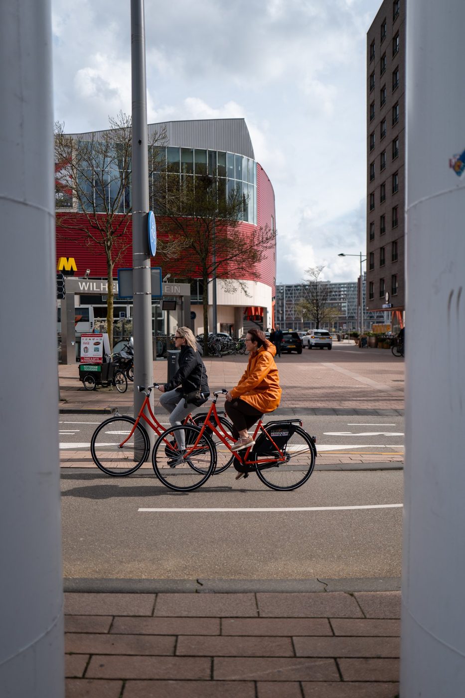 Two cyclists passing near the Wilhelminaplein sign, Rotterdam