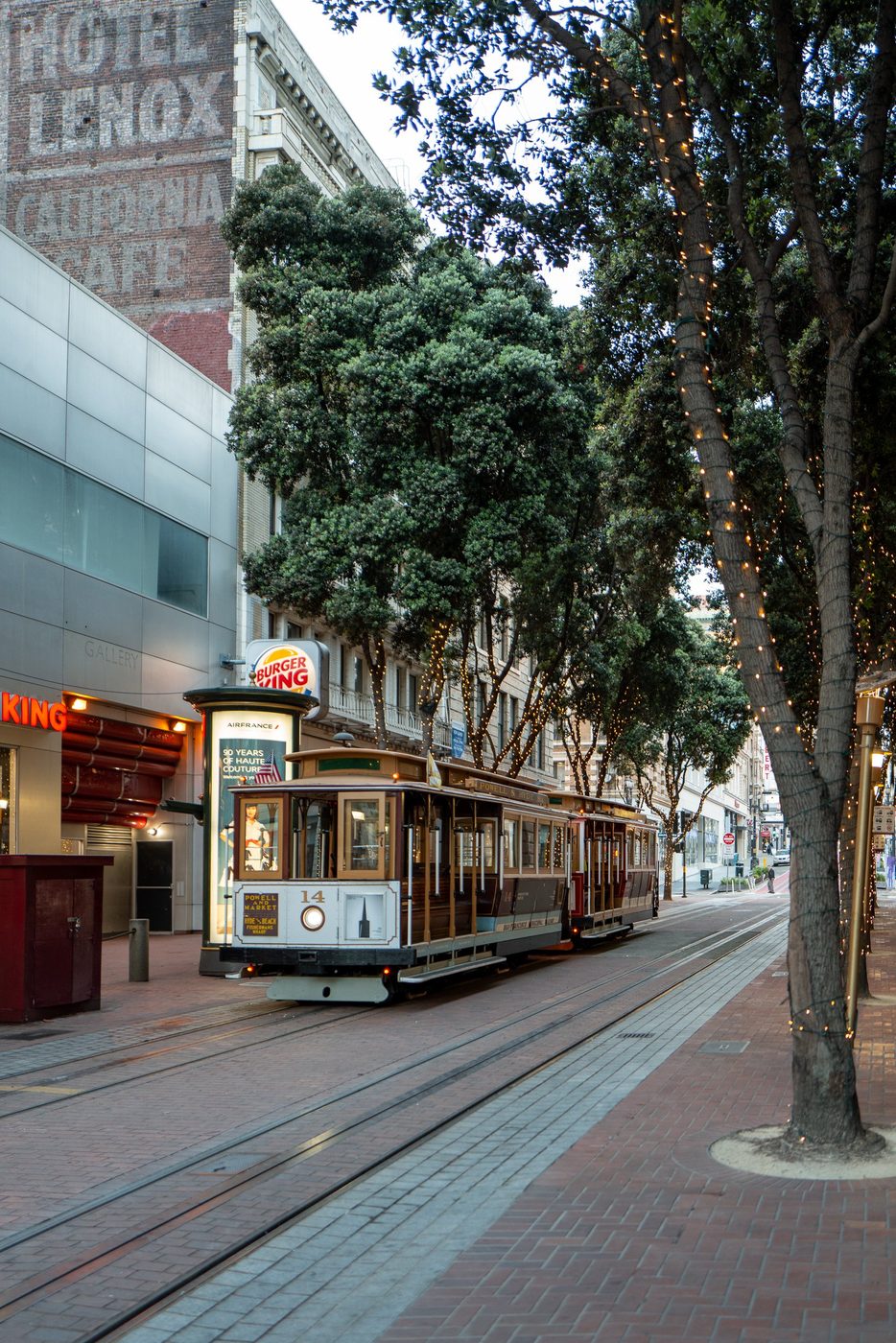 Cable car stopped near Burger King, light garlands in the sidewalk trees, San Francisco