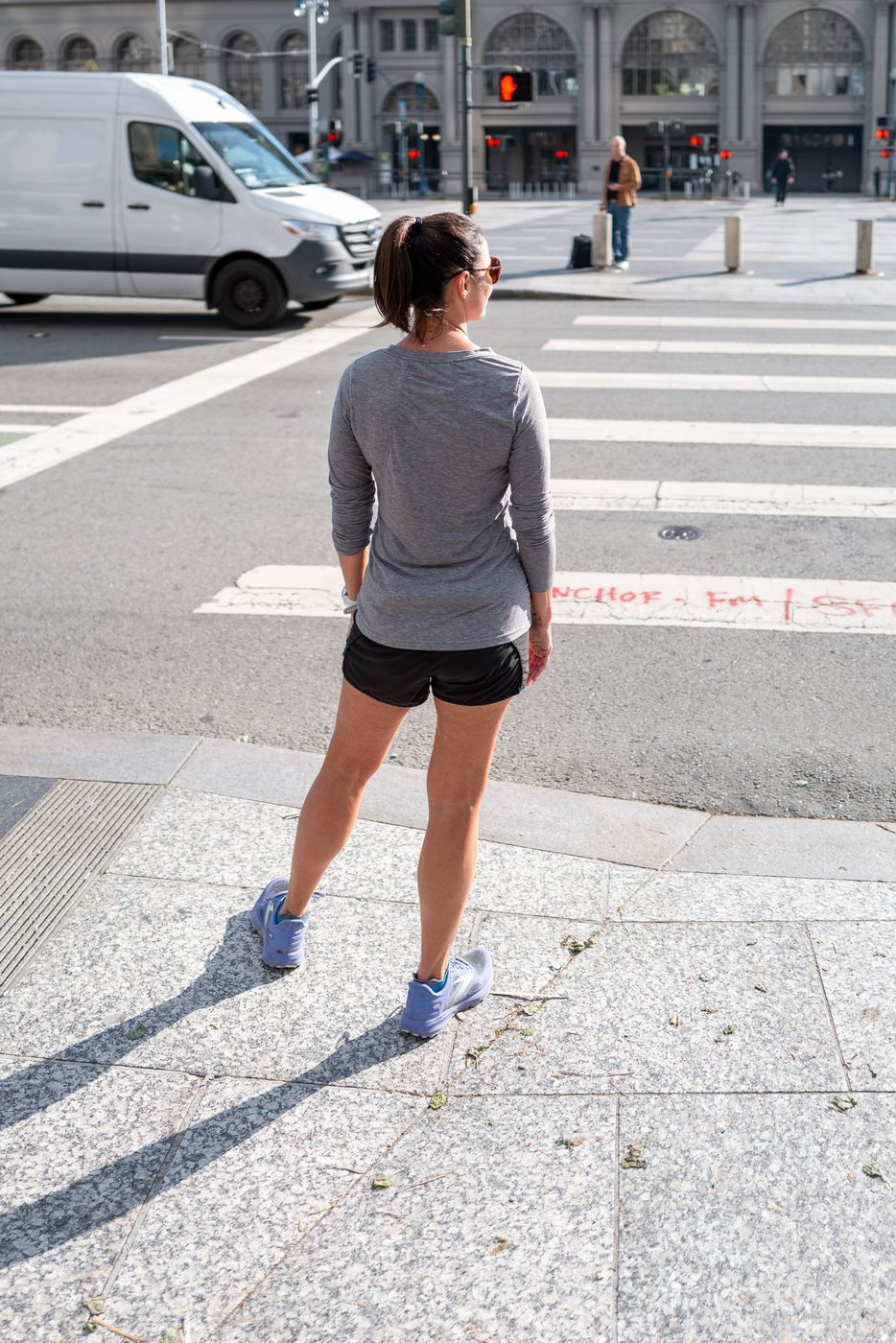 Runner from behind waiting to cross a large sunlit intersection, San Francisco