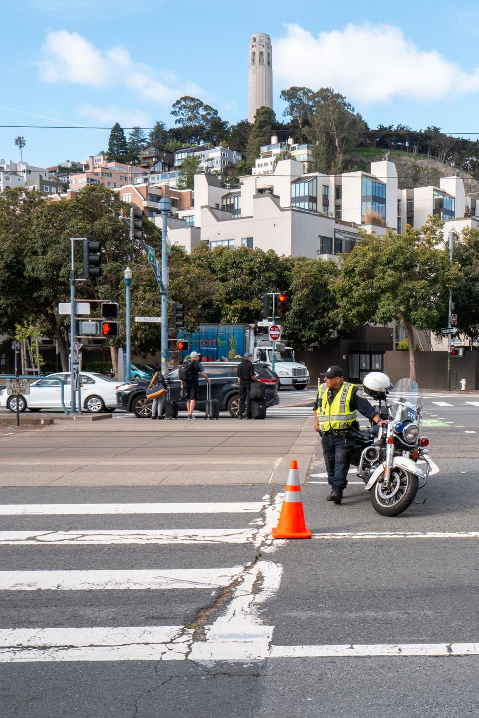 Police motorcycle officer directing traffic at an intersection, Coit Tower in the background, San Francisco