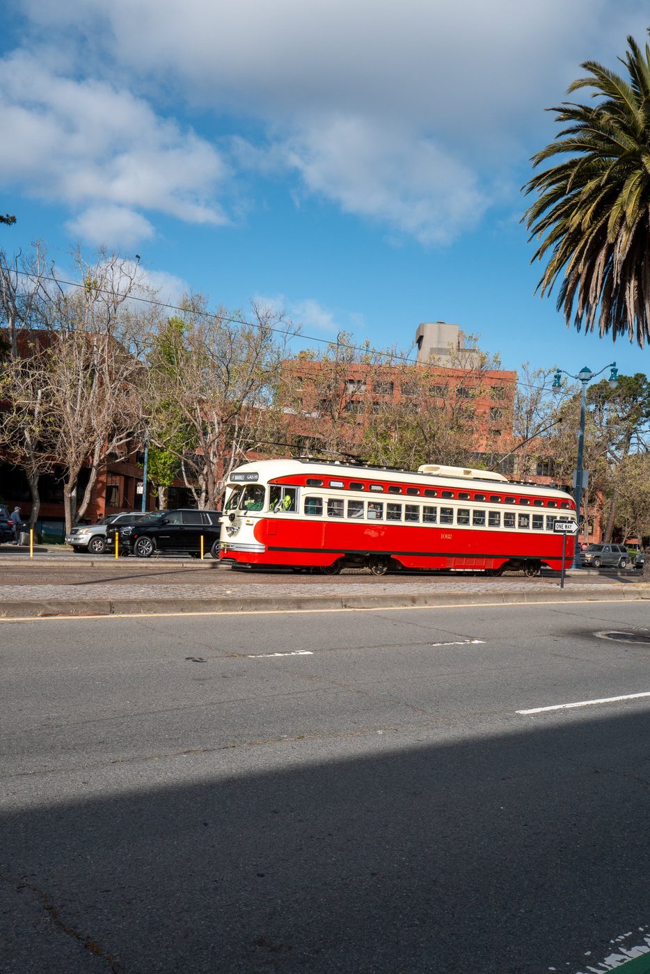 Red and cream streetcar number 1052 under a palm tree, brick building in the background, San Francisco