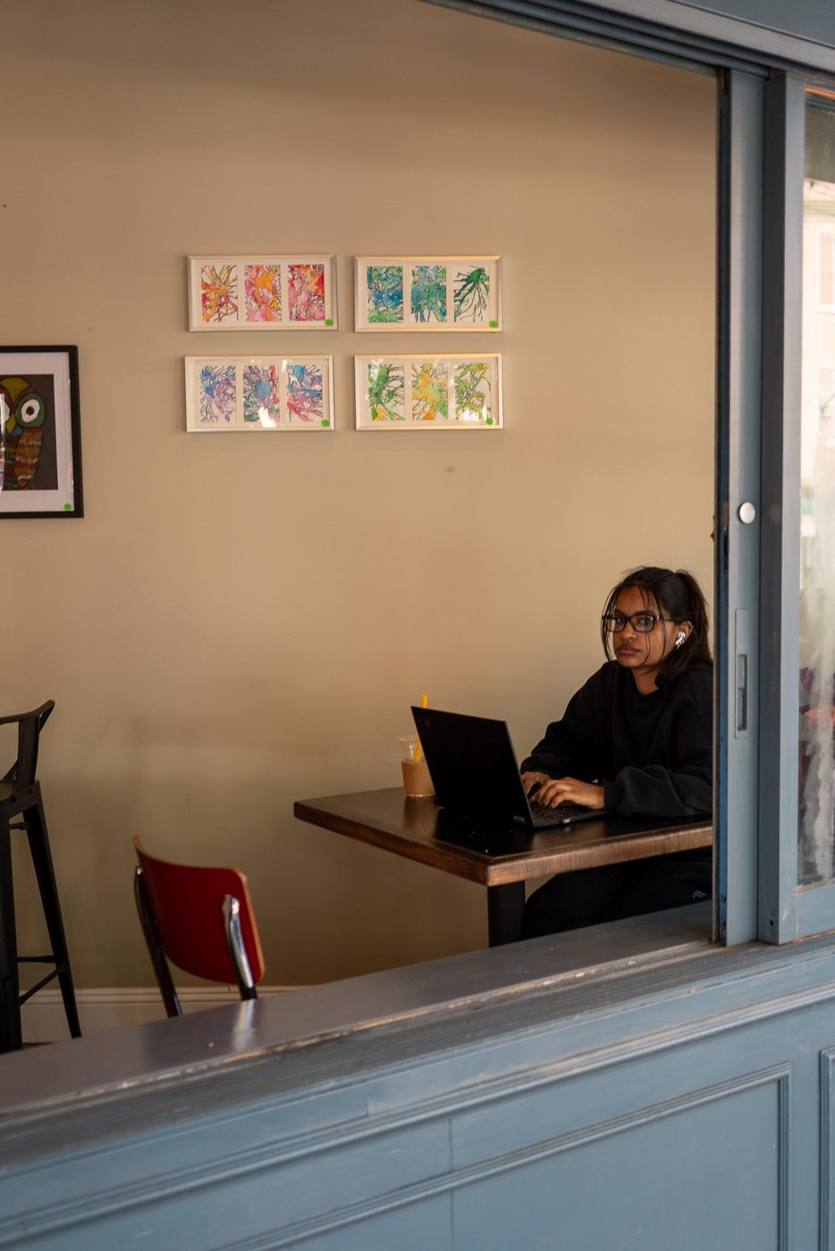 Young woman working on her laptop in a café, seen through the window, San Francisco