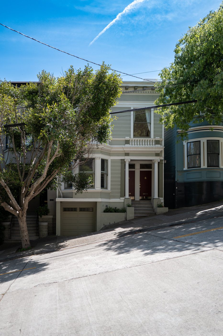 Green Victorian house with a red door on a steep street, San Francisco