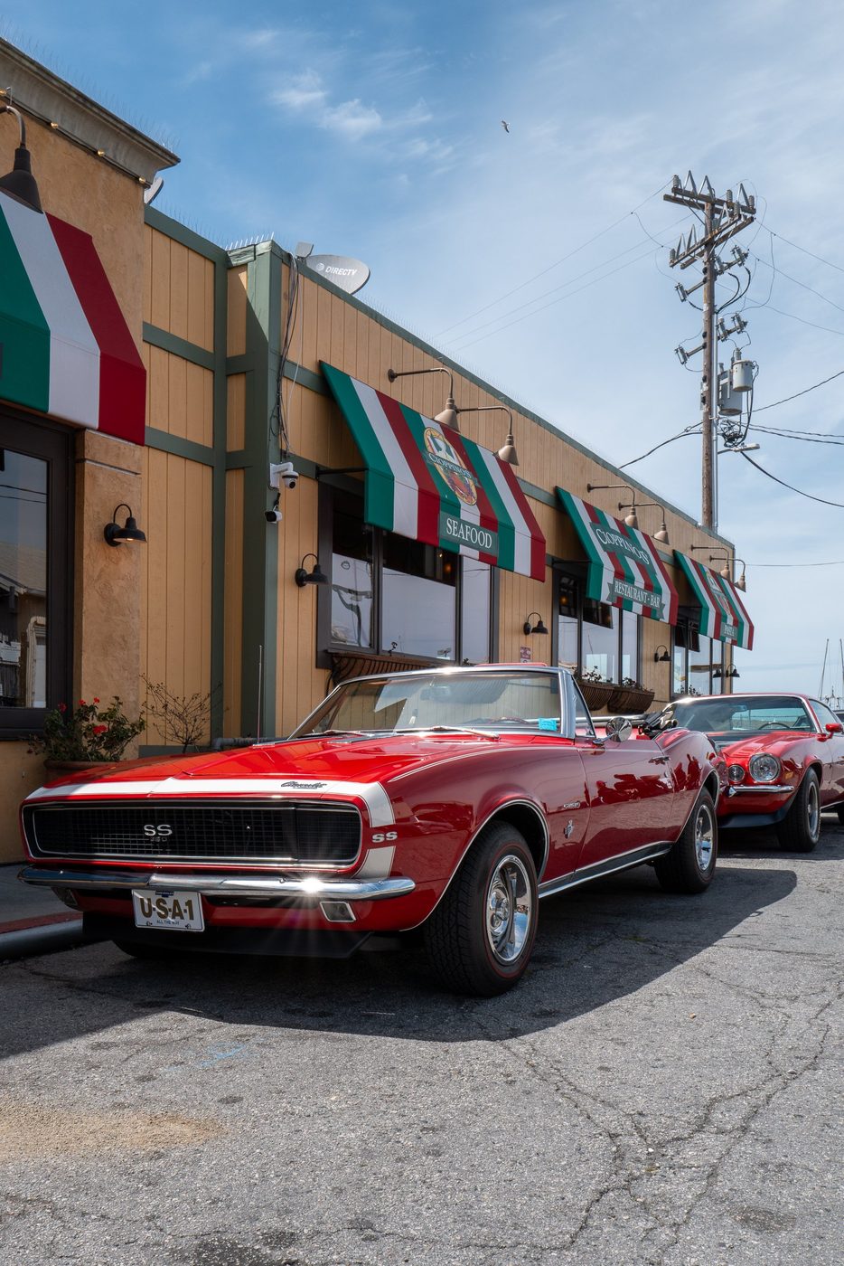 Red convertible Camaro parked in front of an Italian restaurant with striped awnings, San Francisco