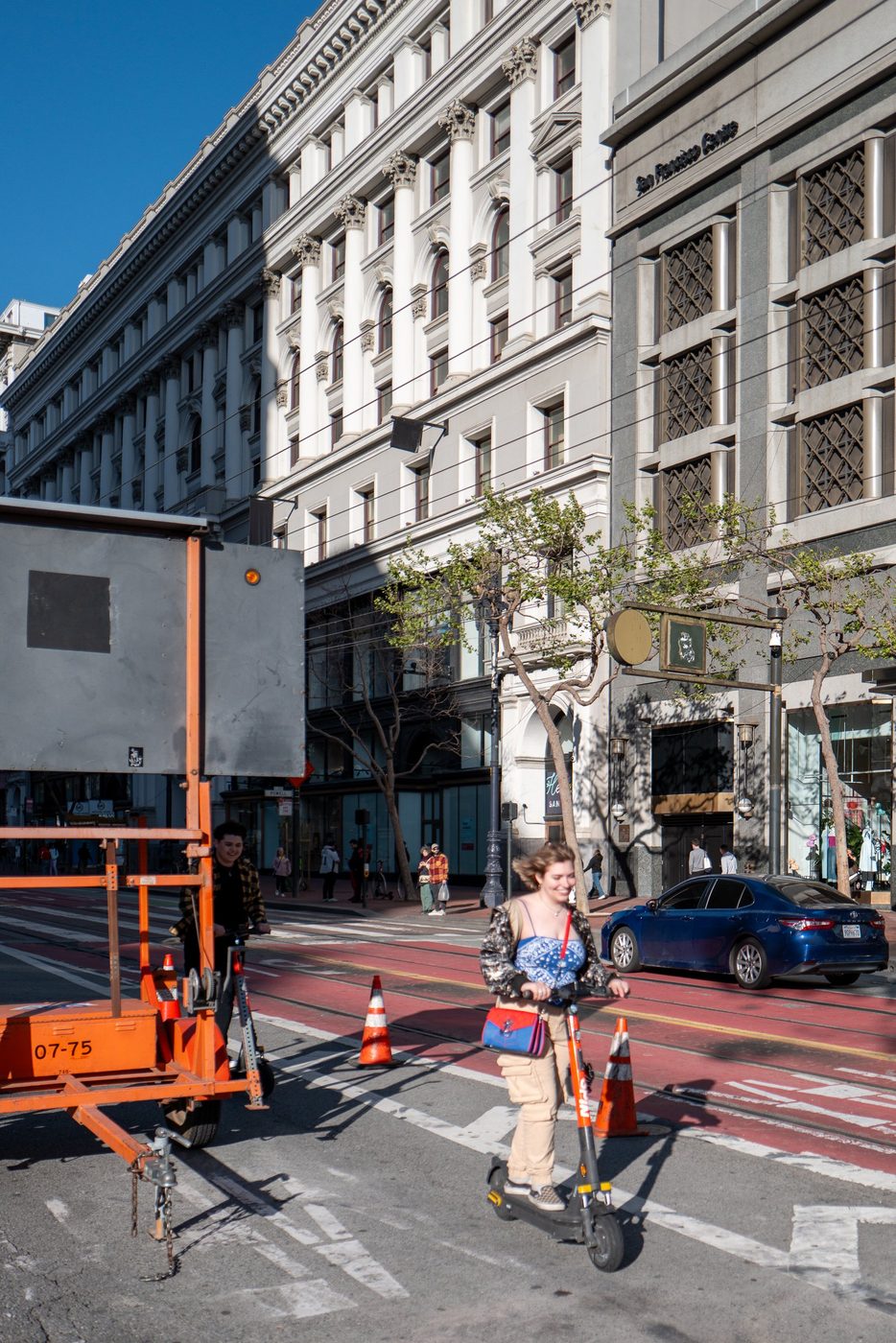 Two young people on electric scooters passing construction equipment, San Francisco