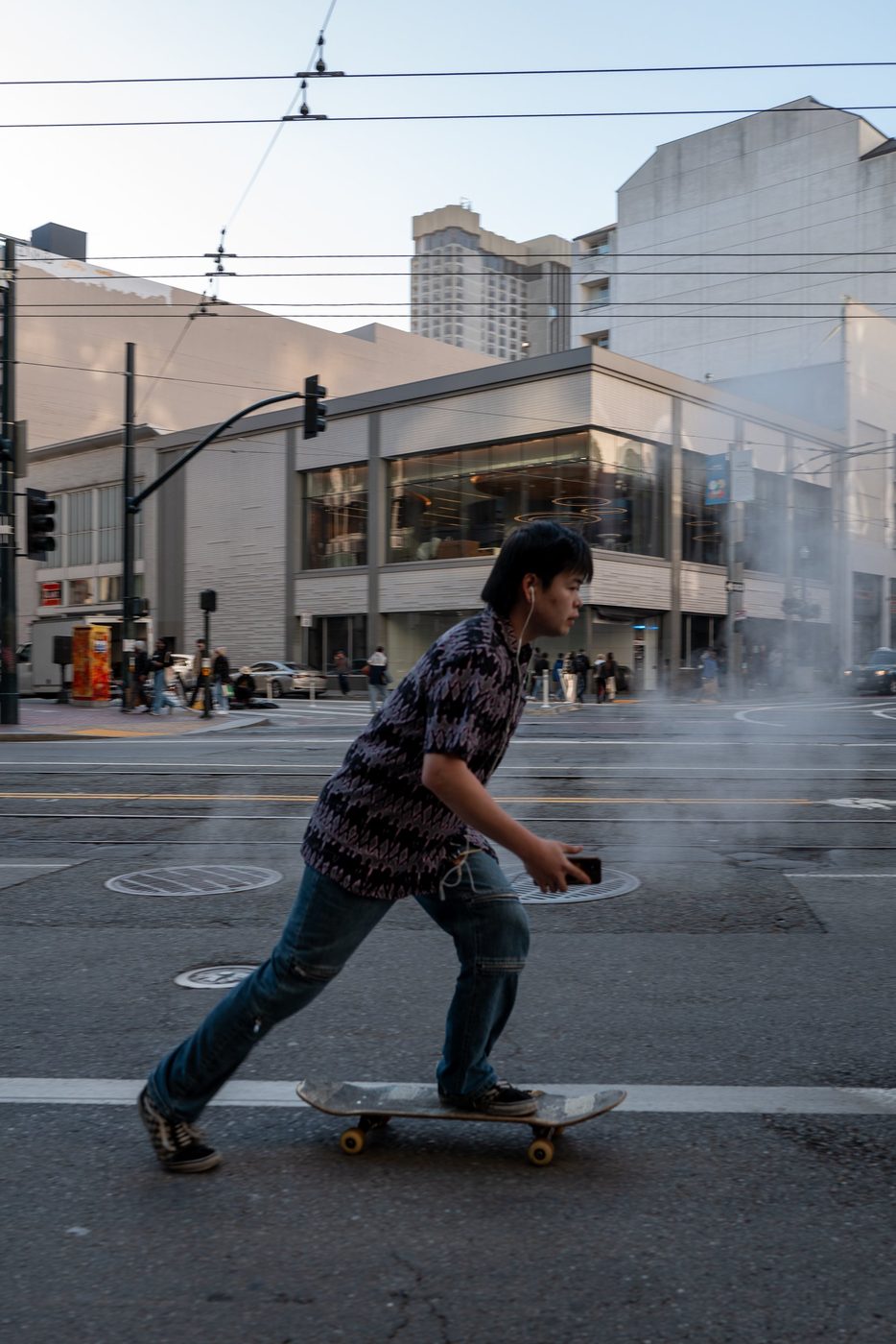 Skater crossing an intersection in the steam of a manhole, San Francisco