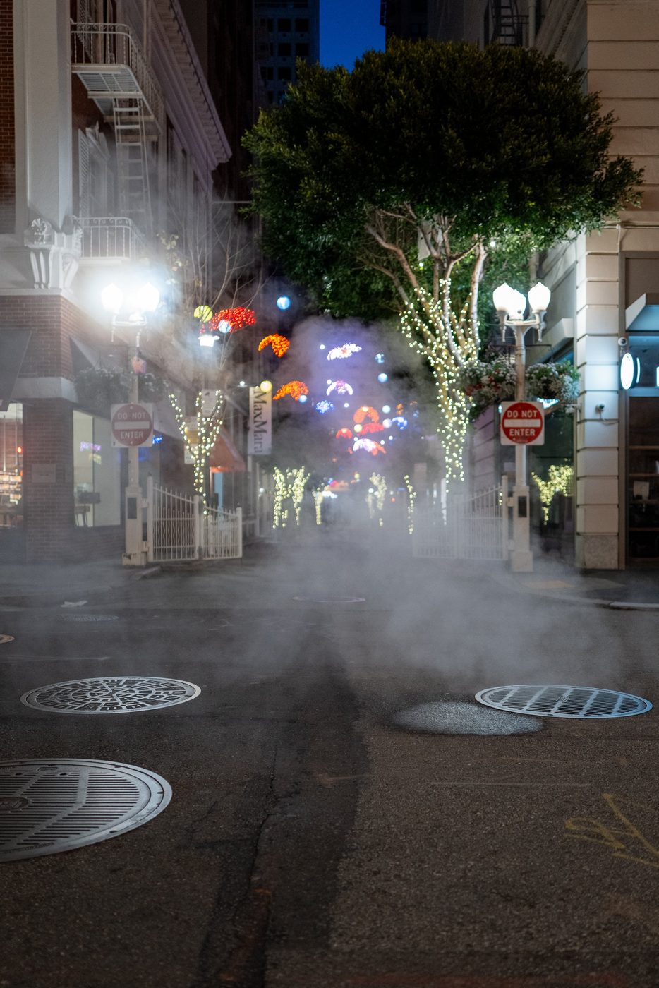 Steam filling an alley decorated with light garlands at night, San Francisco