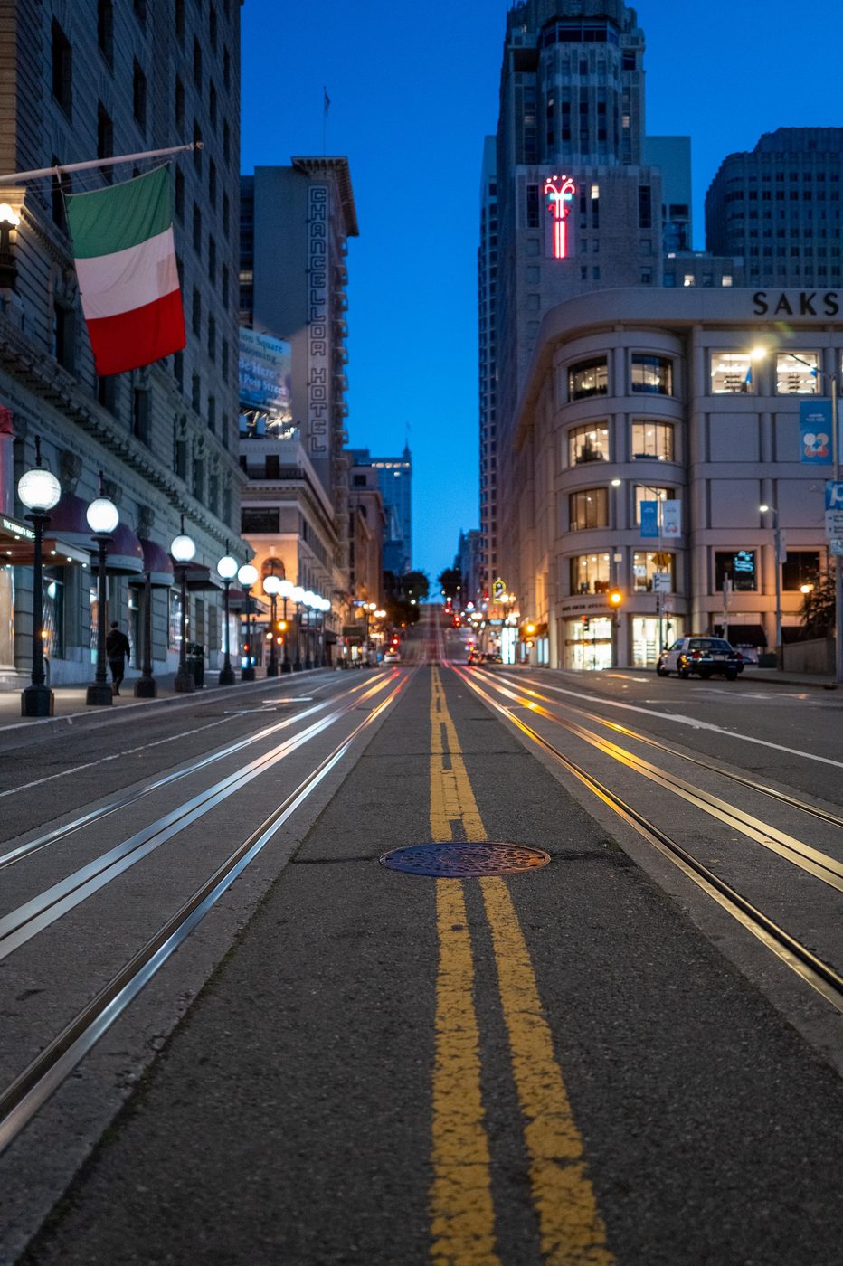 Cable car rails descending California Street between the illuminated hotels at dusk, San Francisco