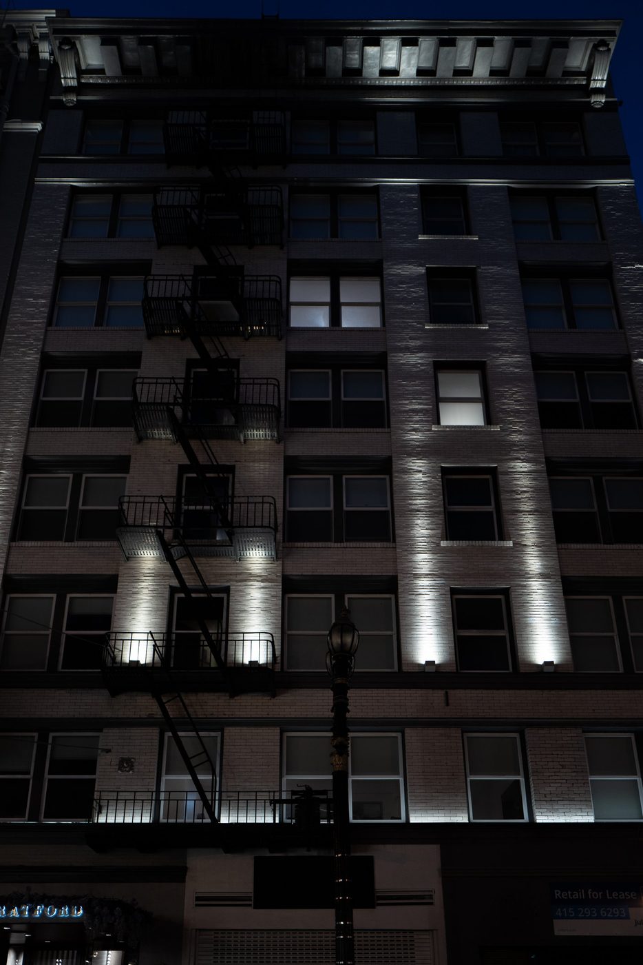 Building façade with fire escapes lit by spotlights at night, San Francisco