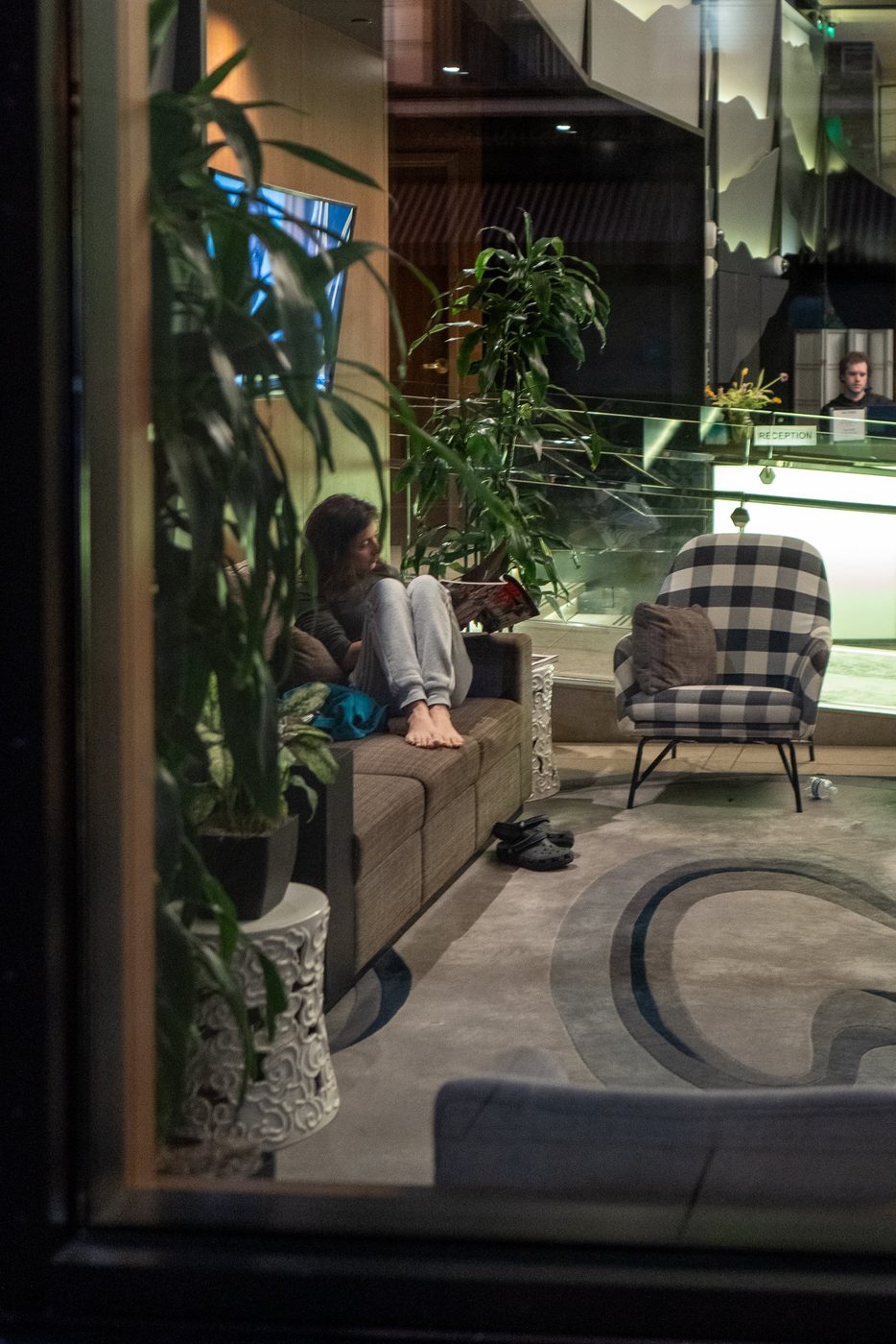Barefoot woman reading on a sofa in a hotel lobby, seen through the window, San Francisco
