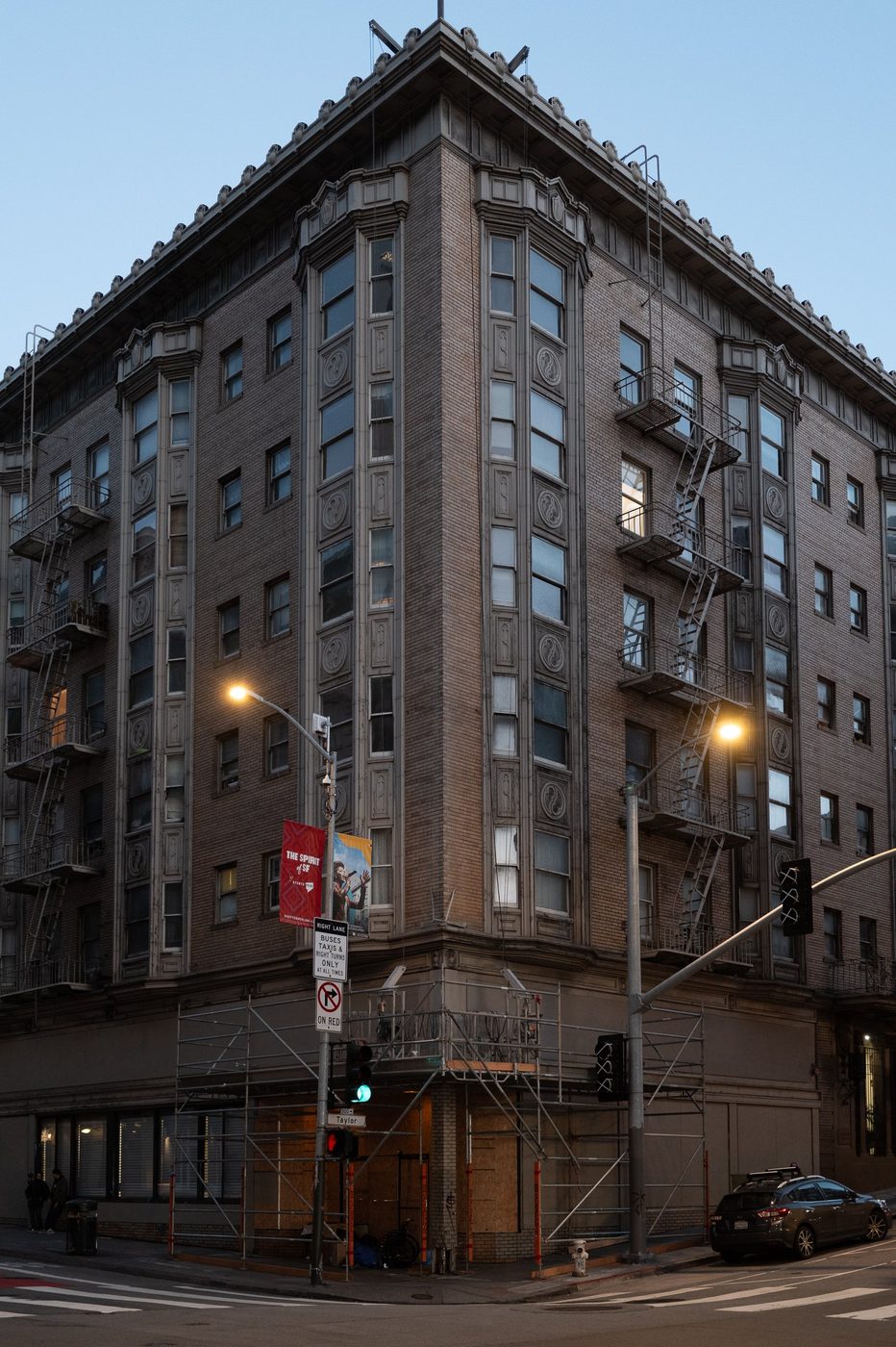 Scaffolded brick building at a street corner, streetlights lit at dusk, San Francisco