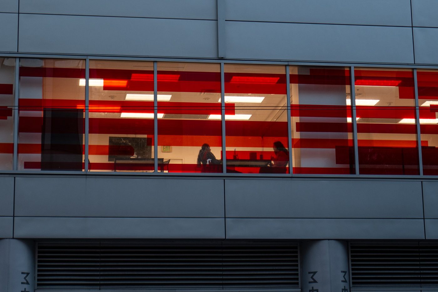 Office lit with red and white stripes, two silhouettes behind the window at night, San Francisco