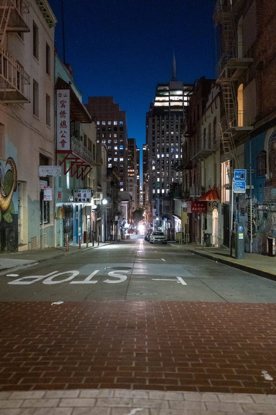 Sloping Chinatown alley at night, STOP marking on the ground and skyscrapers in the distance, San Francisco