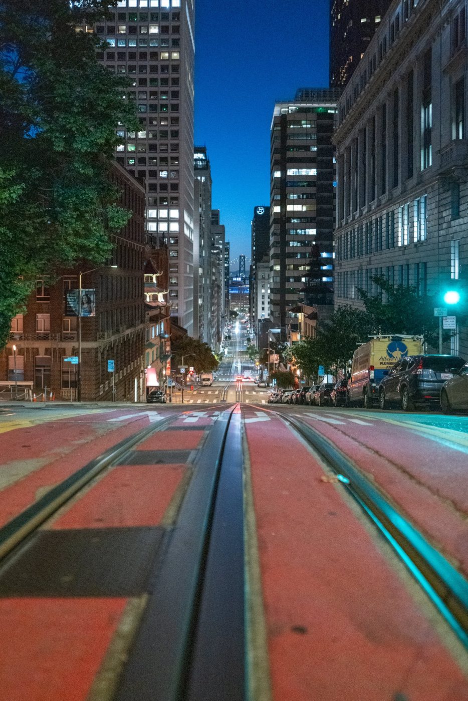 Cable car rails plunging into a sloping street between the illuminated skyscrapers, San Francisco