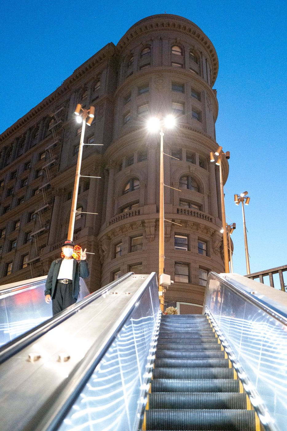 Man making a peace sign on an escalator, classic corner building in the background, San Francisco