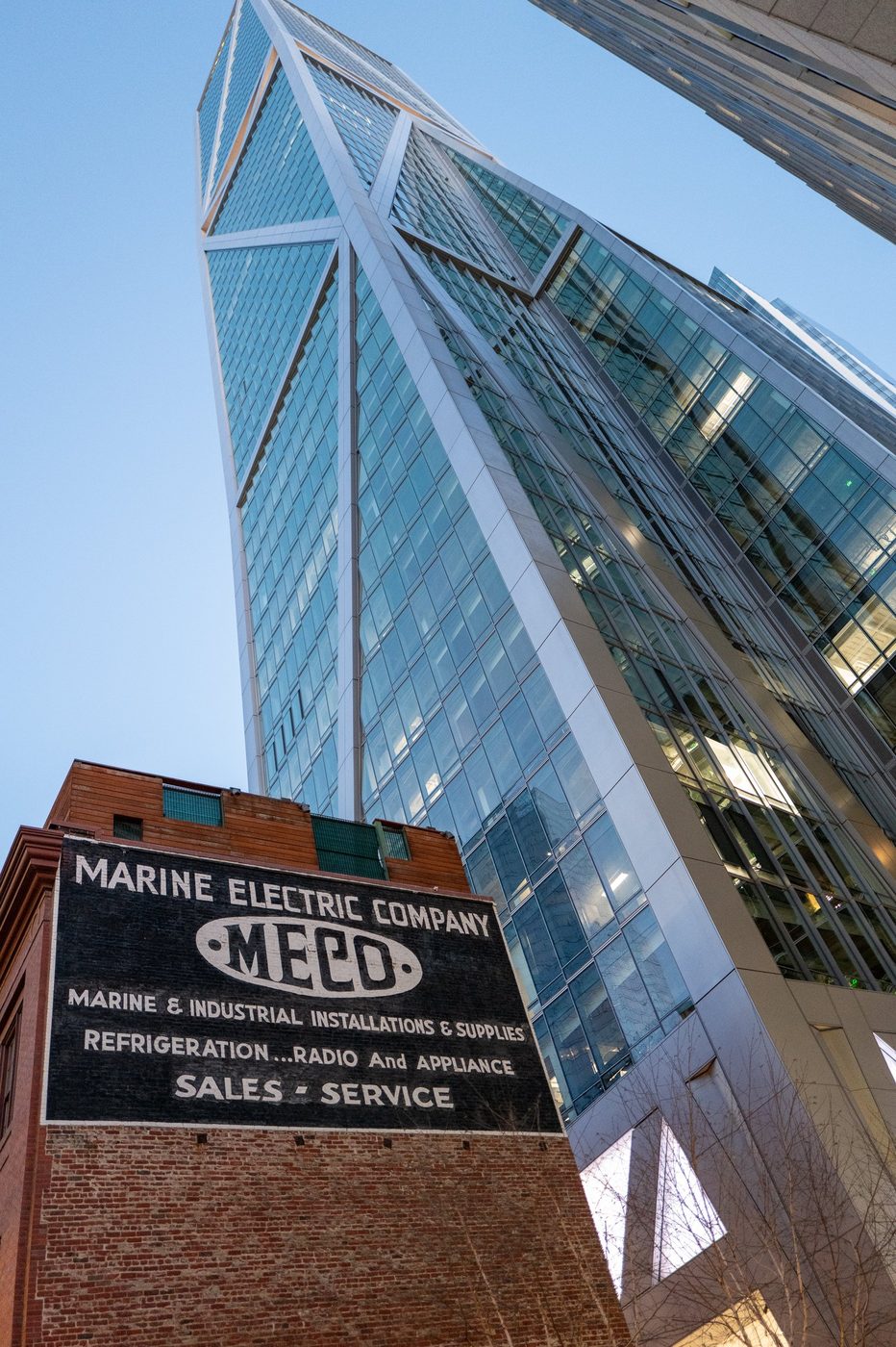 Faceted glass skyscraper looming over an old painted Marine Electric Company sign, San Francisco