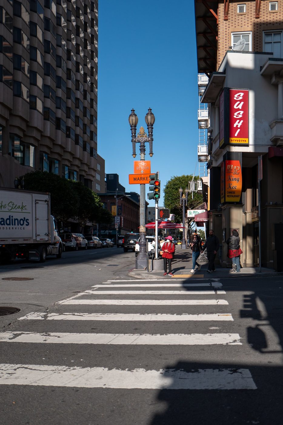 Old streetlamp at the corner of a busy street, Sushi and King Kee signs, passers-by at the light, San Francisco