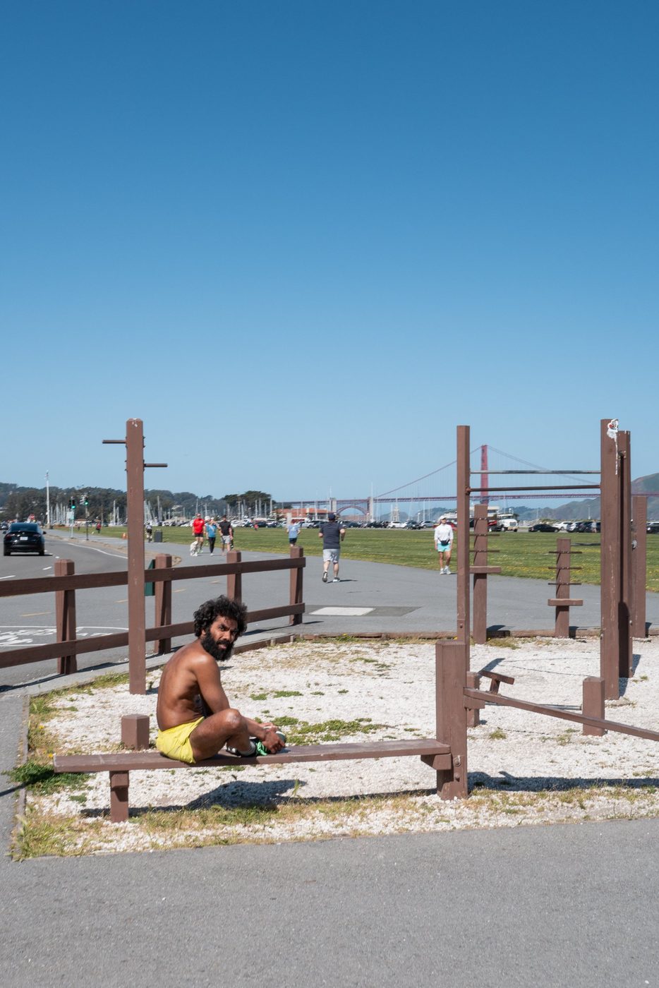 Shirtless man sitting on an outdoor exercise bench, Golden Gate Bridge in the distance, San Francisco