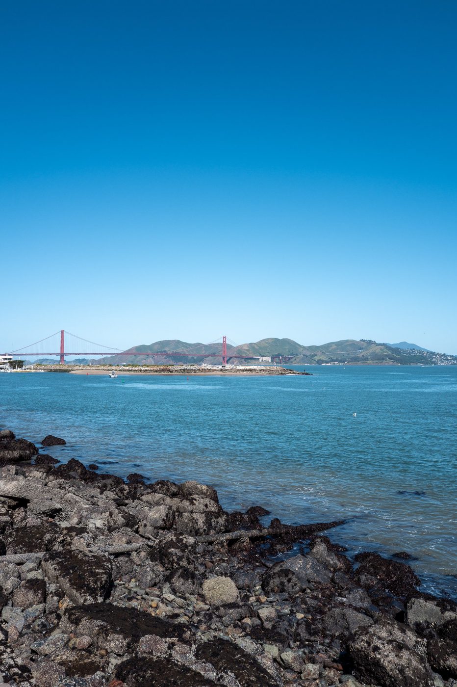 Golden Gate Bridge seen from a rocky shore, deep blue bay, San Francisco