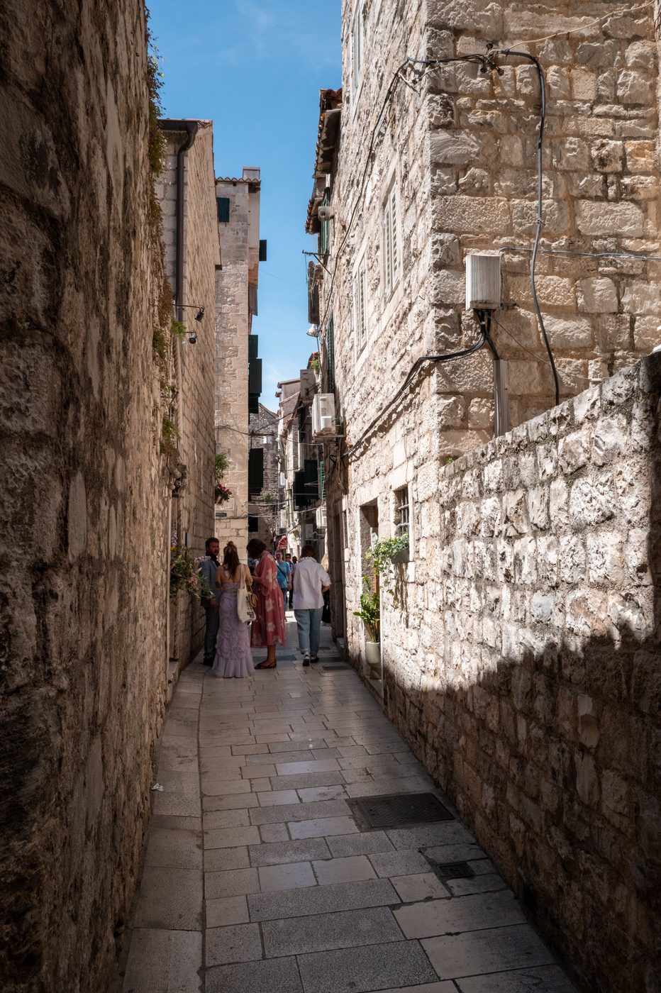 Group of passers-by in a narrow alley lined with stone facades, Split