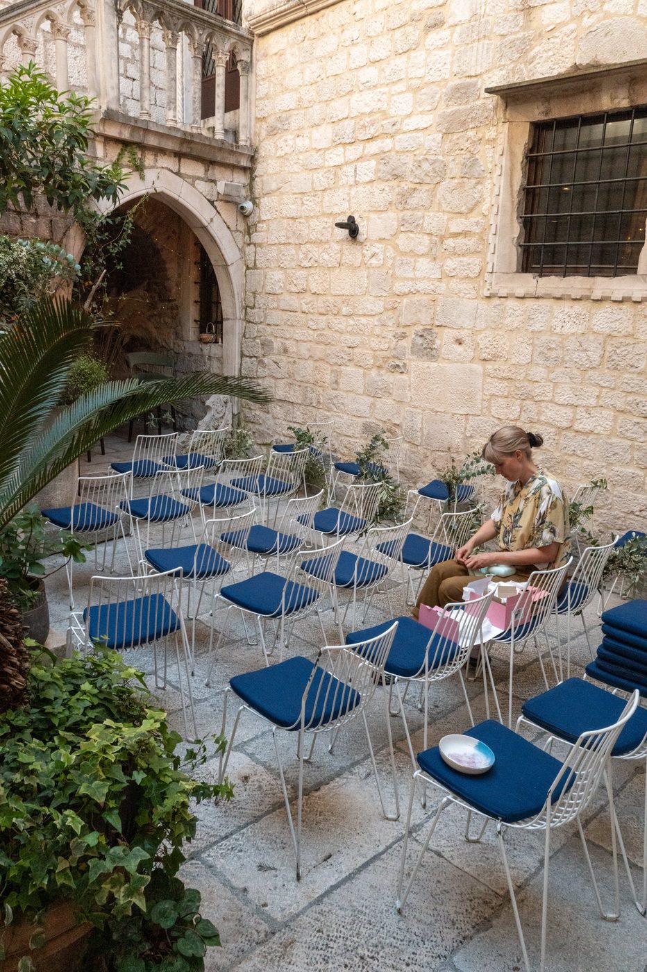Rows of blue chairs set up in a stone courtyard for an event, Split