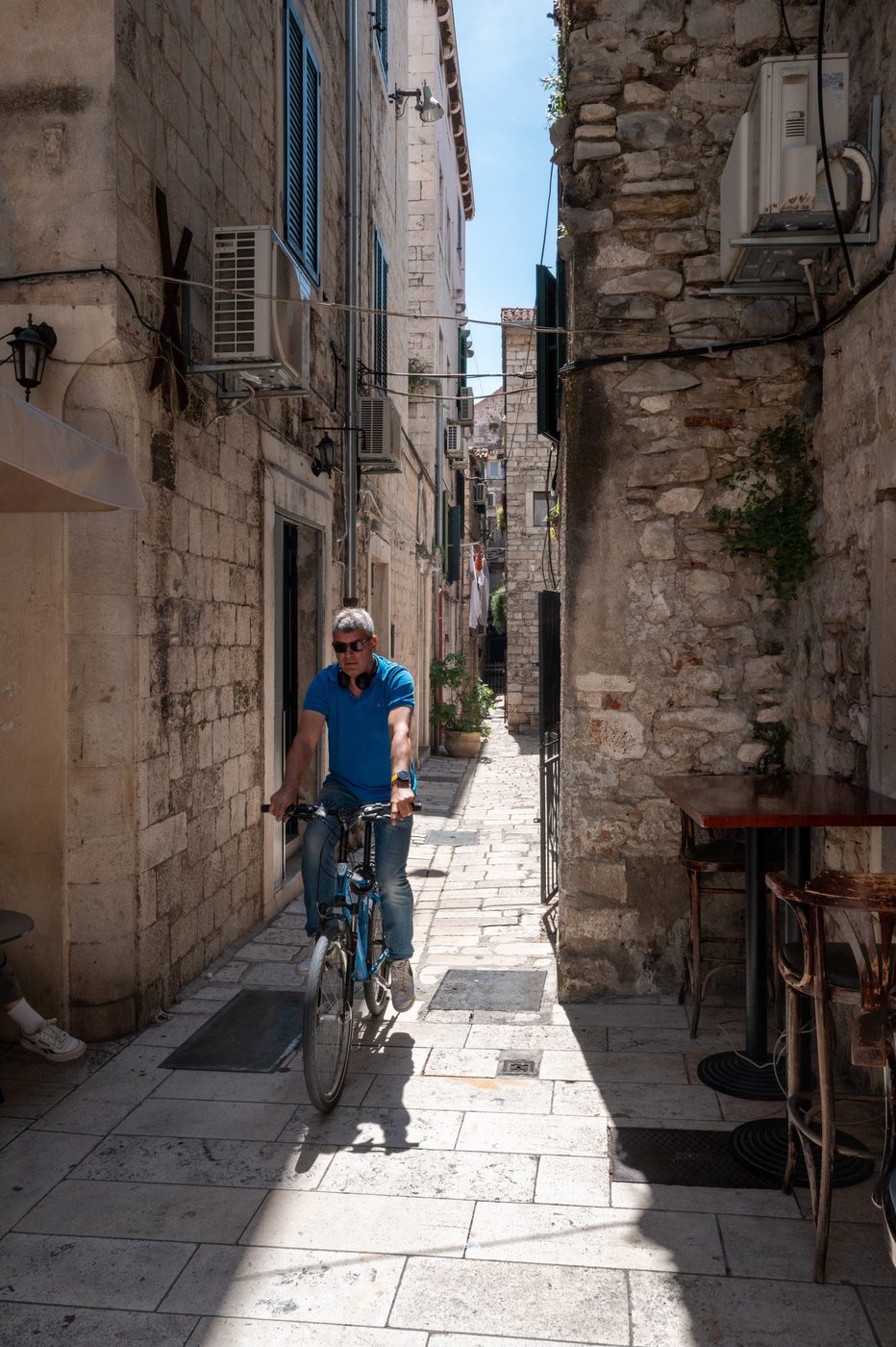 Cyclist in a blue polo shirt crossing a narrow alley, Split