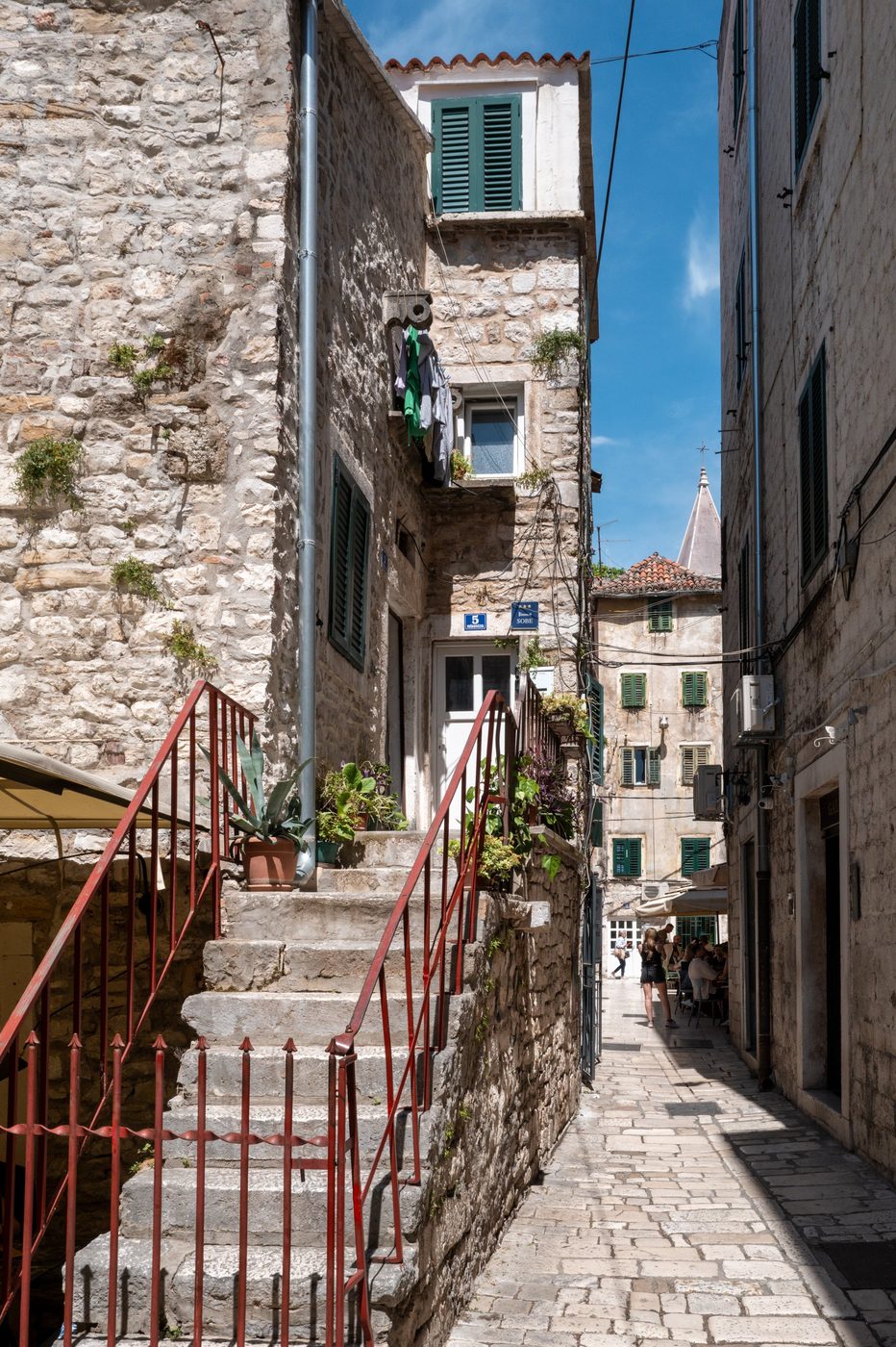 Staircase with a red railing leading to a bustling alley, Split