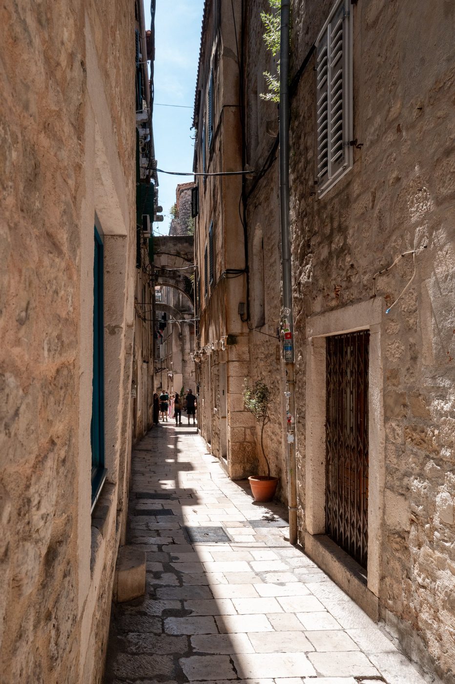 Narrow dead-end lined with flower pots leading to a small square, Split