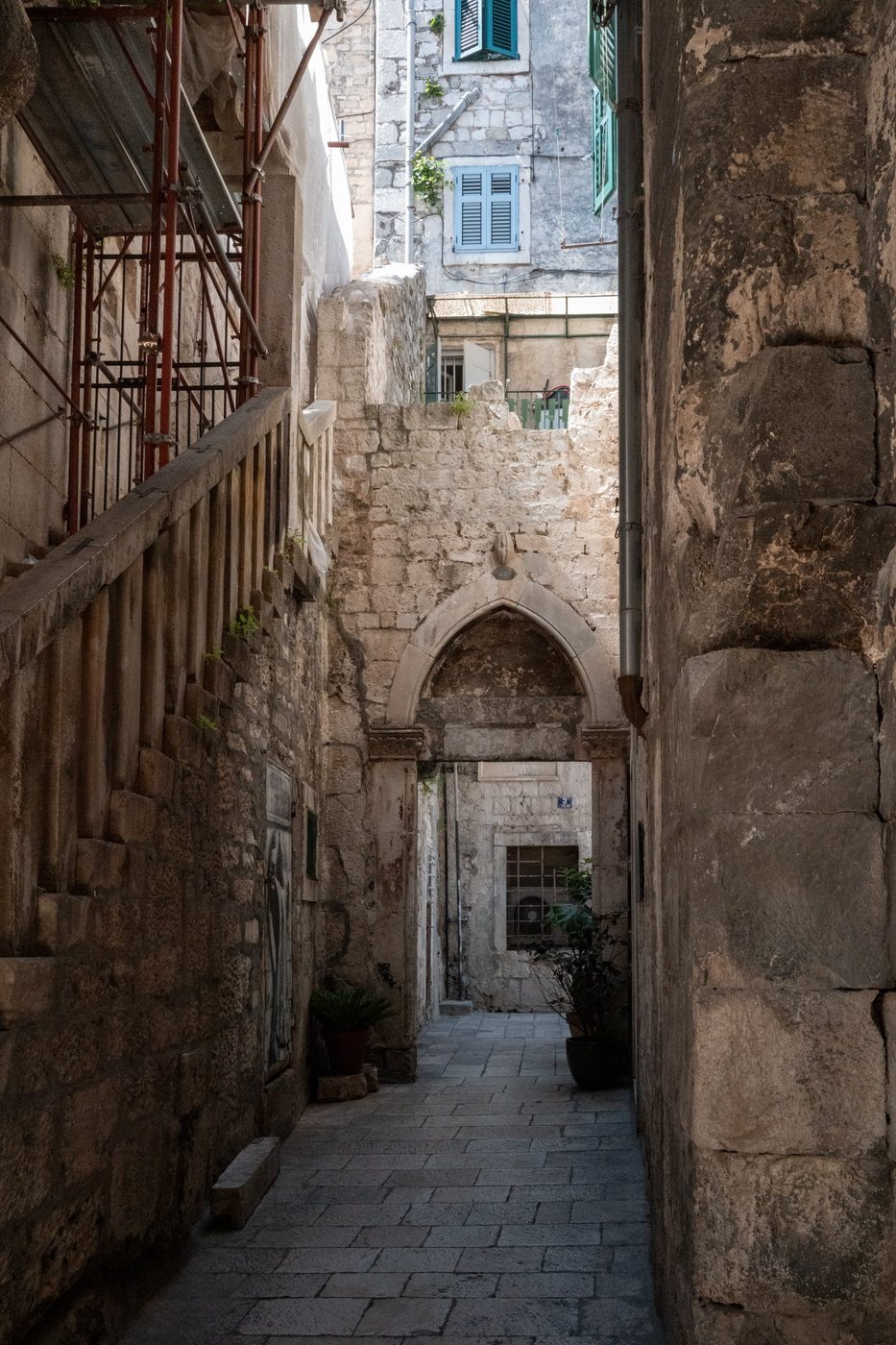 Red scaffolding and Gothic arch at the end of a shaded alley, Split